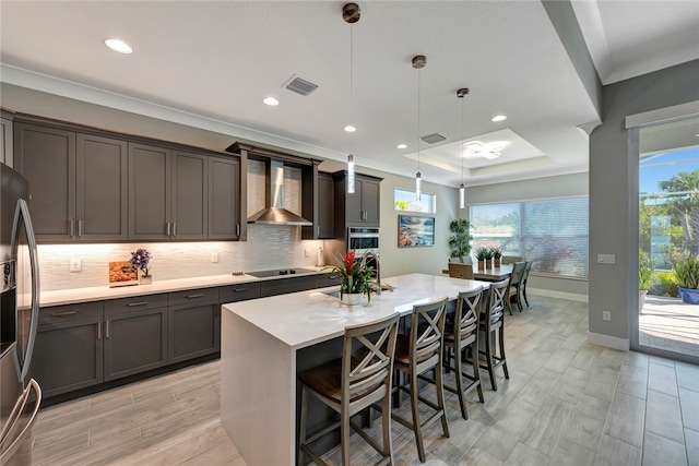 kitchen featuring a kitchen bar, stainless steel appliances, wall chimney range hood, pendant lighting, and a center island