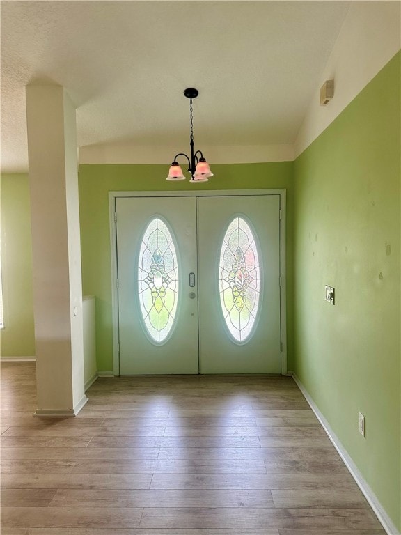 foyer entrance with vaulted ceiling, a chandelier, light hardwood / wood-style flooring, and french doors