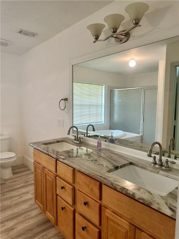 bathroom with walk in shower, a textured ceiling, hardwood / wood-style floors, vanity, and toilet