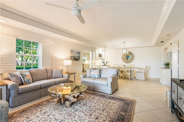 living room featuring light tile patterned floors, a ceiling fan, baseboards, ornamental molding, and a tray ceiling