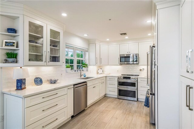 kitchen with appliances with stainless steel finishes, light wood-type flooring, white cabinetry, and a sink