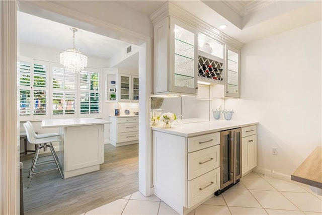 kitchen with a breakfast bar area, light countertops, visible vents, glass insert cabinets, and beverage cooler