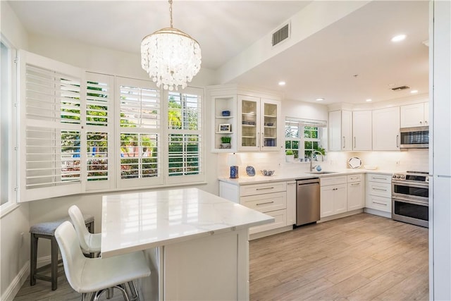 kitchen featuring light wood finished floors, tasteful backsplash, visible vents, appliances with stainless steel finishes, and a sink