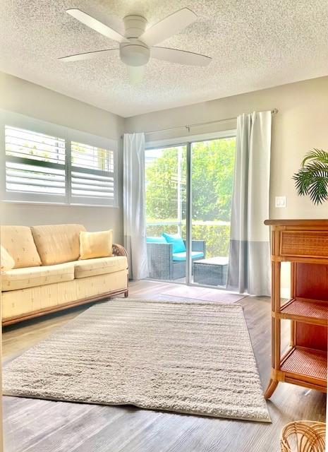 living area with a ceiling fan, wood finished floors, a wealth of natural light, and a textured ceiling