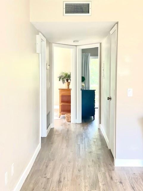 corridor with baseboards, visible vents, and light wood-type flooring