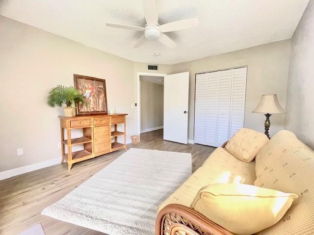 living area with a ceiling fan, wood finished floors, visible vents, and baseboards