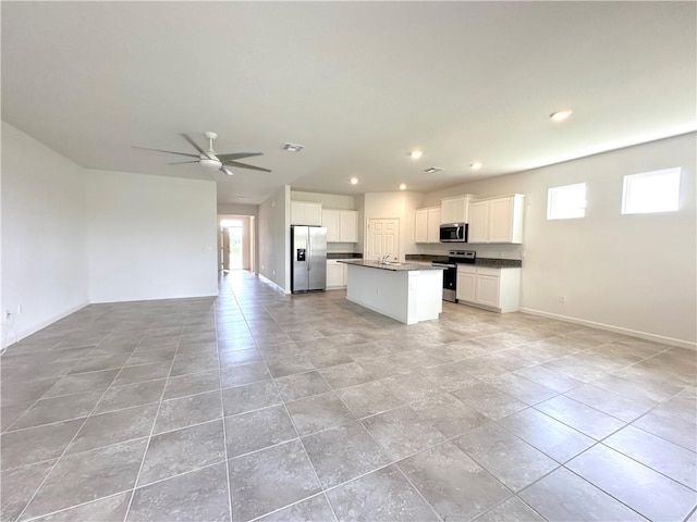 kitchen with stainless steel appliances, dark countertops, open floor plan, white cabinets, and an island with sink