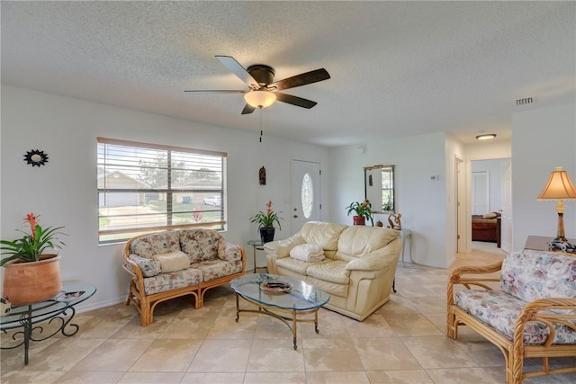 living area featuring a textured ceiling, a ceiling fan, visible vents, light tile patterned flooring, and baseboards