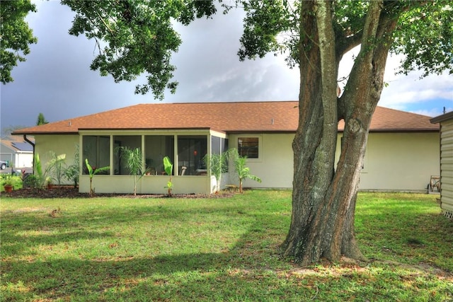 view of front of home with a front yard, roof with shingles, a sunroom, and stucco siding