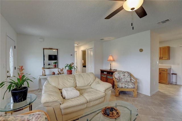living area featuring baseboards, light tile patterned floors, a textured ceiling, visible vents, and ceiling fan