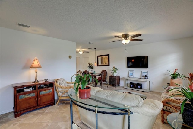 living room with a textured ceiling, light tile patterned floors, a ceiling fan, and visible vents
