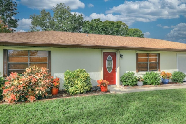 ranch-style home with a front yard, stucco siding, and roof with shingles