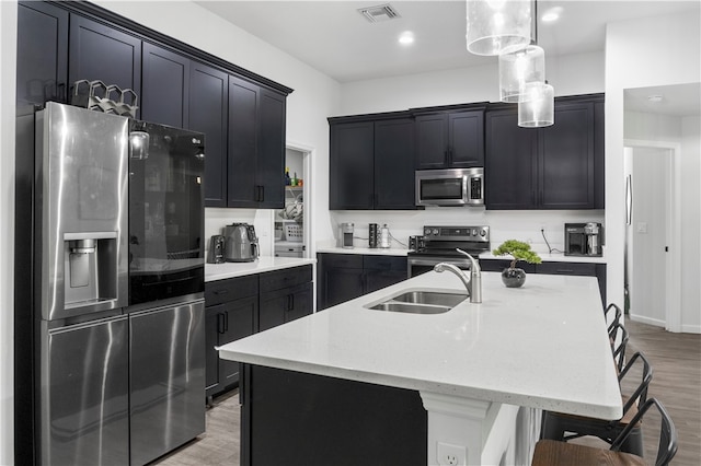 kitchen featuring stainless steel appliances, sink, a kitchen island with sink, light hardwood / wood-style flooring, and decorative light fixtures