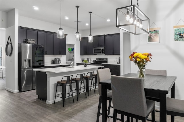 kitchen featuring pendant lighting, appliances with stainless steel finishes, wood-type flooring, and a center island with sink