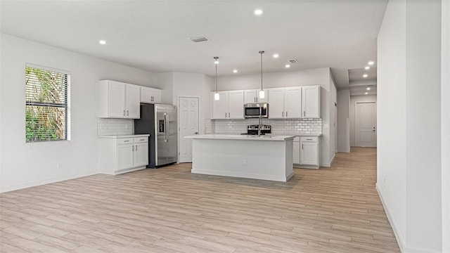 kitchen with pendant lighting, light hardwood / wood-style flooring, appliances with stainless steel finishes, an island with sink, and white cabinets