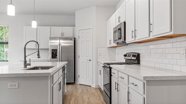 kitchen with pendant lighting, sink, appliances with stainless steel finishes, white cabinetry, and a center island with sink