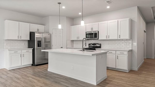 kitchen featuring appliances with stainless steel finishes, a kitchen island with sink, white cabinets, and decorative light fixtures