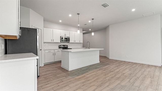 kitchen featuring appliances with stainless steel finishes, decorative light fixtures, an island with sink, sink, and white cabinets