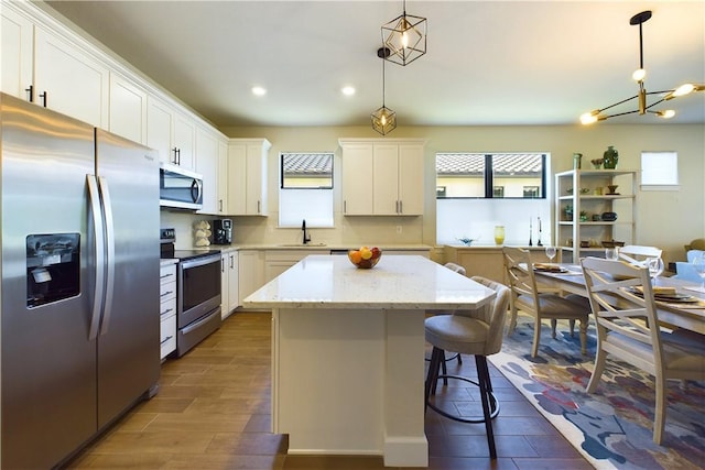 kitchen with white cabinets, appliances with stainless steel finishes, a center island, and decorative light fixtures