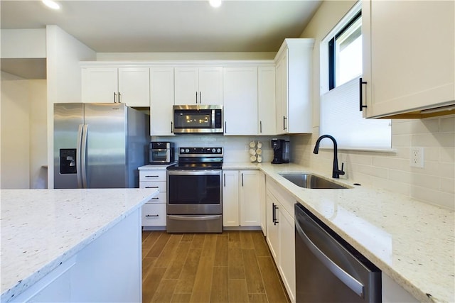 kitchen with white cabinets, appliances with stainless steel finishes, light stone counters, and sink