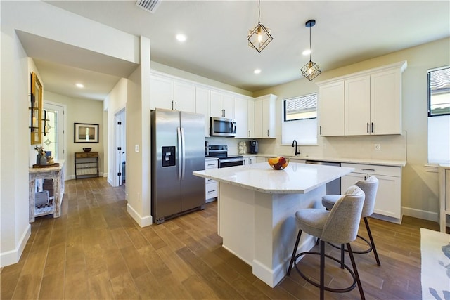 kitchen with white cabinets, decorative light fixtures, a center island, and appliances with stainless steel finishes