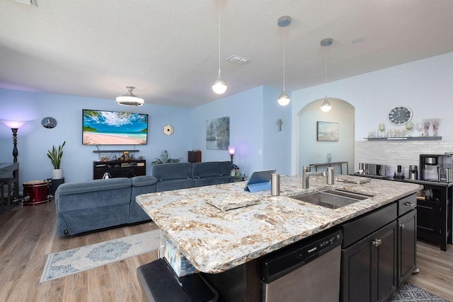 kitchen with sink, a center island with sink, light hardwood / wood-style flooring, stainless steel dishwasher, and light stone countertops