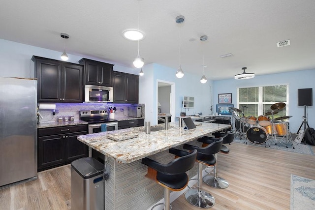 kitchen featuring appliances with stainless steel finishes, a breakfast bar, hanging light fixtures, and a center island with sink