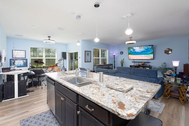 kitchen with pendant lighting, sink, dishwasher, a kitchen island with sink, and light stone counters