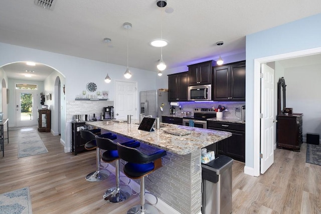 kitchen featuring stainless steel appliances, a kitchen bar, decorative light fixtures, and a center island with sink