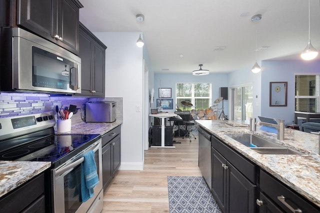 kitchen featuring pendant lighting, sink, stainless steel appliances, decorative backsplash, and light wood-type flooring