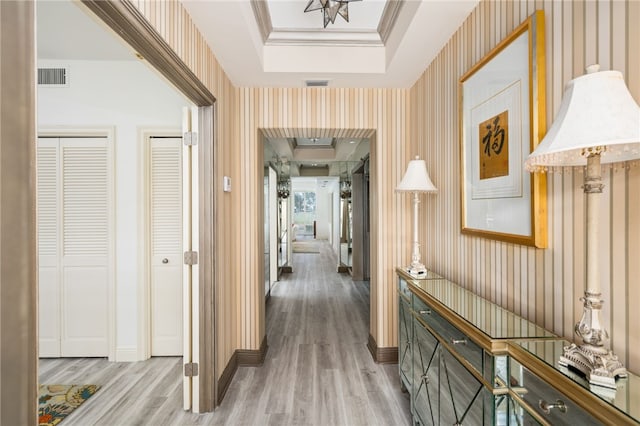 hall with a raised ceiling, crown molding, and light hardwood / wood-style floors