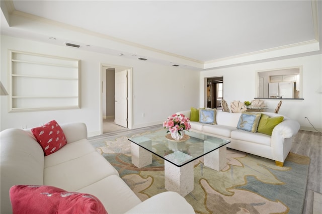 living room featuring built in shelves, light hardwood / wood-style floors, a raised ceiling, and ornamental molding