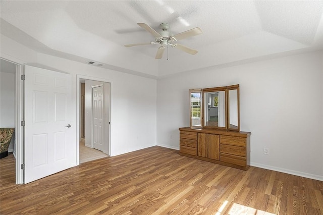 interior space featuring a raised ceiling, ceiling fan, a textured ceiling, and light wood-type flooring