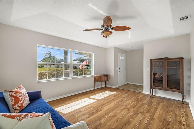 unfurnished living room featuring ceiling fan, a tray ceiling, a textured ceiling, and hardwood / wood-style flooring