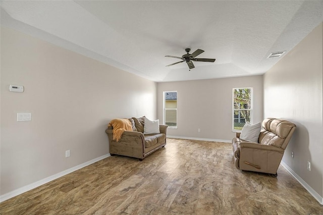 living area with a raised ceiling and ceiling fan