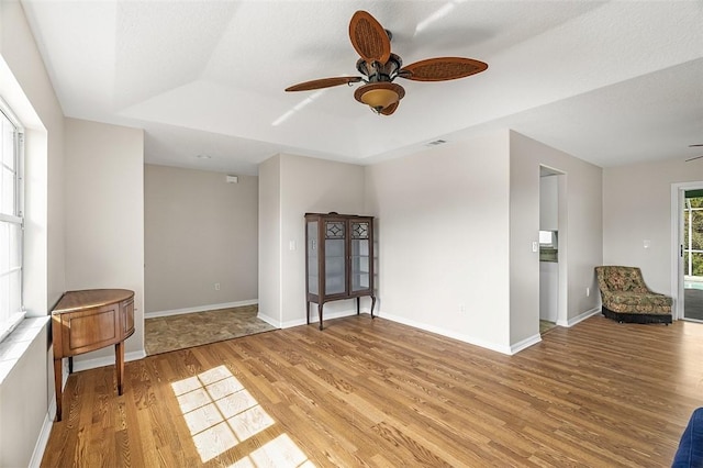 empty room with a raised ceiling, ceiling fan, and light hardwood / wood-style flooring