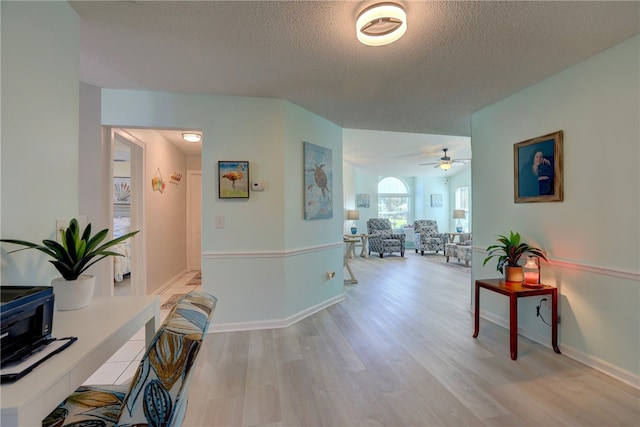 hall with baseboards, light wood-style floors, and a textured ceiling