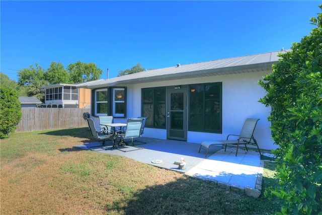 rear view of house featuring stucco siding, a lawn, fence, a sunroom, and a patio area