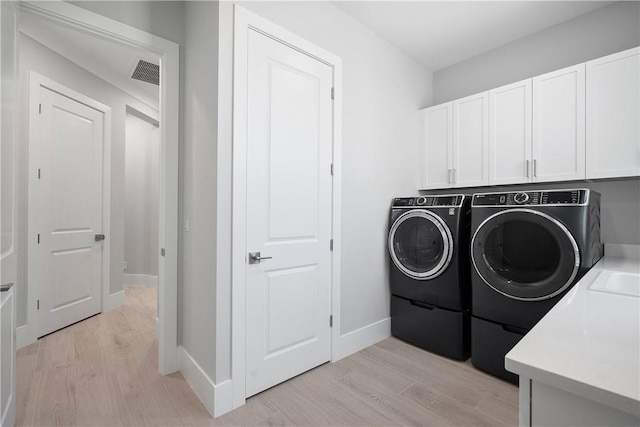 129 Strand Dr, Vero Beach, FL 32963 - laundry area featuring visible vents, washer and clothes dryer, light wood finished floors, and cabinet space