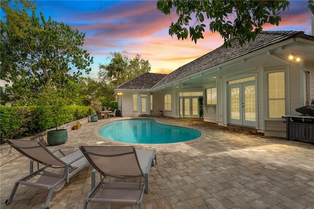 pool at dusk featuring an outdoor pool, french doors, and a patio