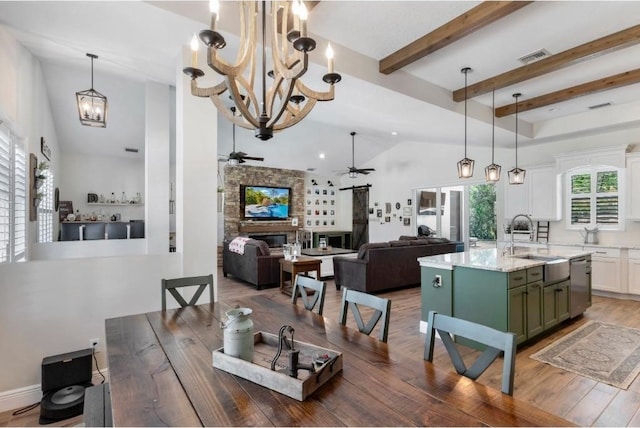 dining area with sink, hardwood / wood-style floors, vaulted ceiling with beams, a fireplace, and ceiling fan with notable chandelier