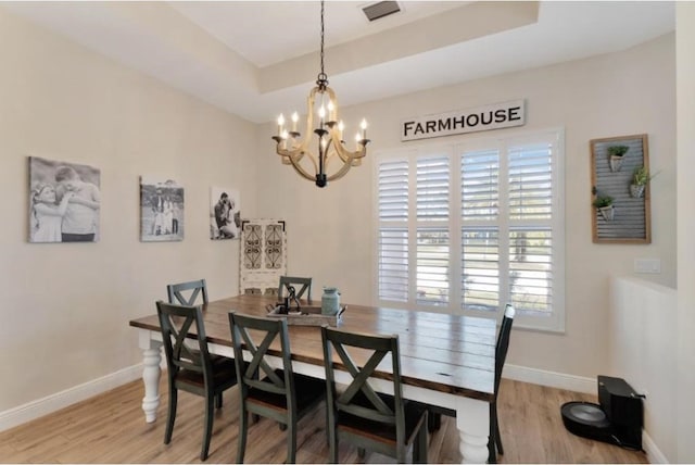 dining area featuring a raised ceiling, a chandelier, and light hardwood / wood-style floors