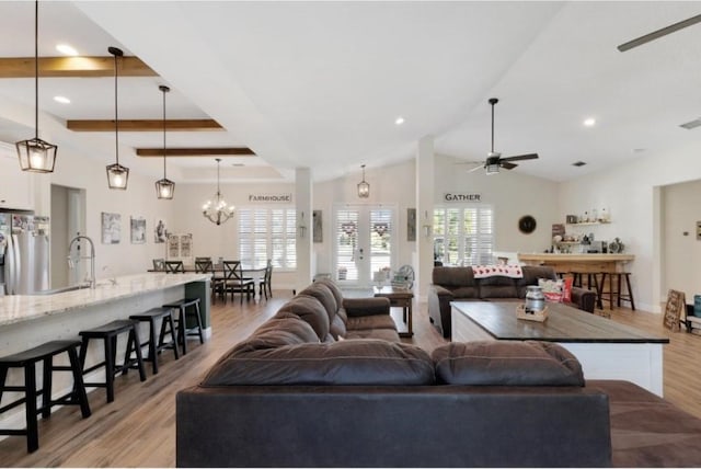 living room featuring sink, high vaulted ceiling, light hardwood / wood-style flooring, a tray ceiling, and ceiling fan with notable chandelier