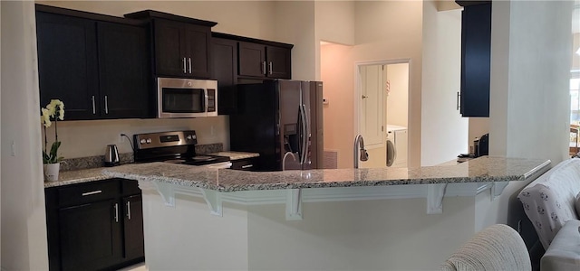 kitchen featuring a breakfast bar area, light stone countertops, a peninsula, separate washer and dryer, and appliances with stainless steel finishes