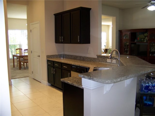 kitchen with a breakfast bar, a sink, light stone counters, a peninsula, and dishwashing machine