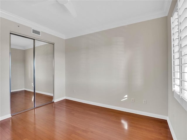 unfurnished bedroom with ceiling fan, a closet, crown molding, and hardwood / wood-style flooring