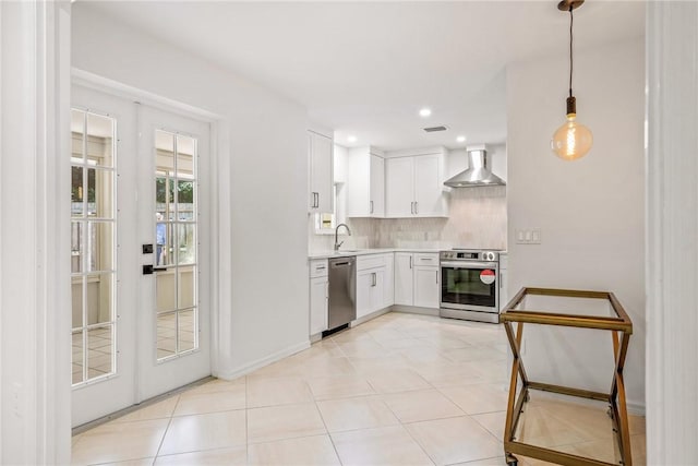 kitchen with backsplash, white cabinetry, decorative light fixtures, wall chimney range hood, and stainless steel appliances