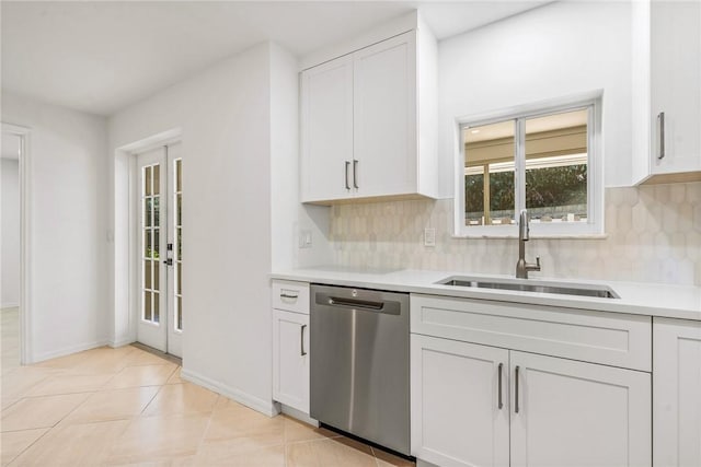 kitchen with stainless steel dishwasher, backsplash, light tile patterned floors, sink, and white cabinetry