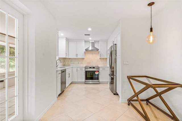 kitchen featuring white cabinets, stainless steel appliances, pendant lighting, and wall chimney range hood