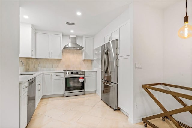 kitchen with appliances with stainless steel finishes, wall chimney range hood, decorative backsplash, pendant lighting, and white cabinetry